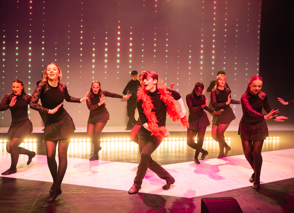 Students perform a dance routine, one with a feather boa around their neck.