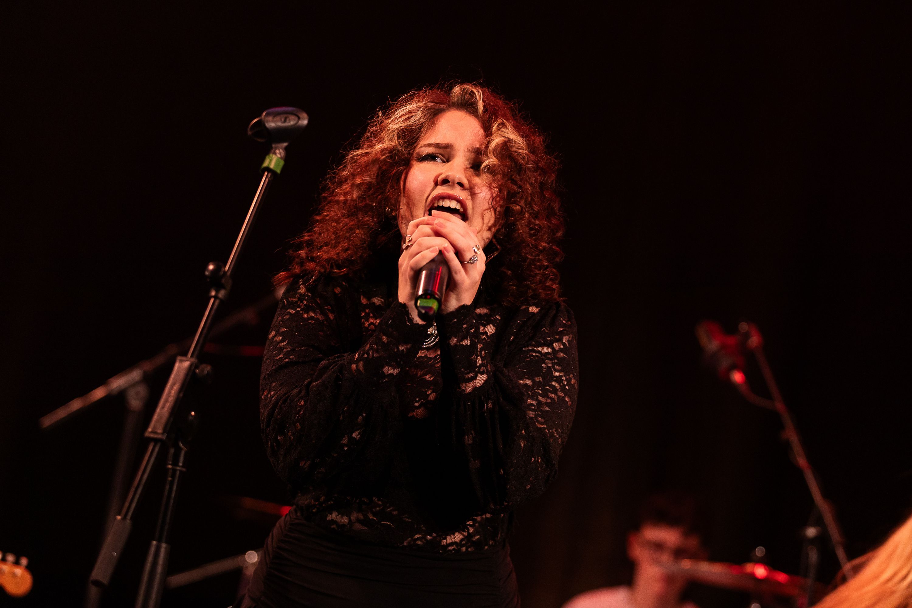 A student vocalist singing on stage accompanied by the rest of the band. 
