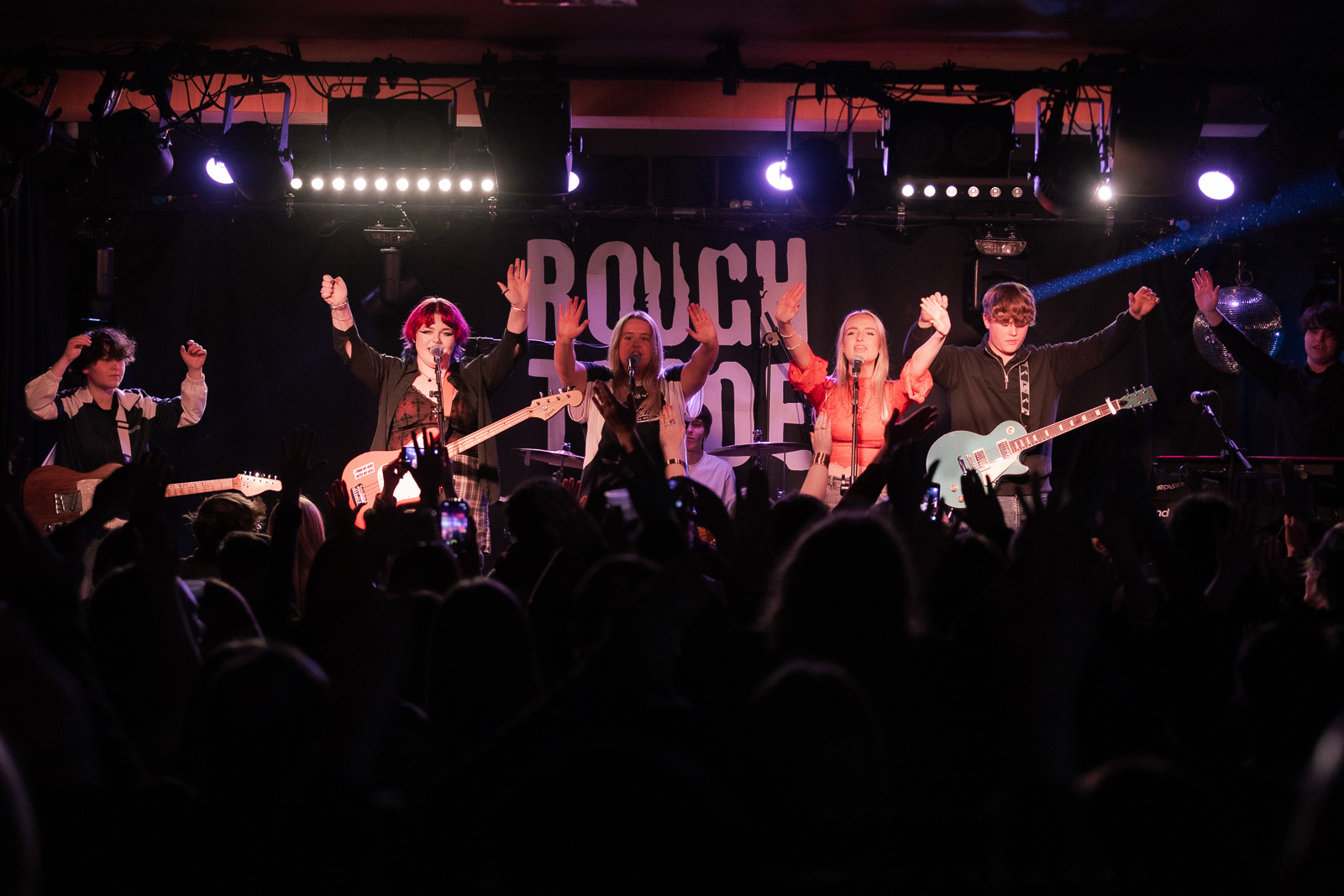 A band on stage holding their hands up to the audience as they perform.