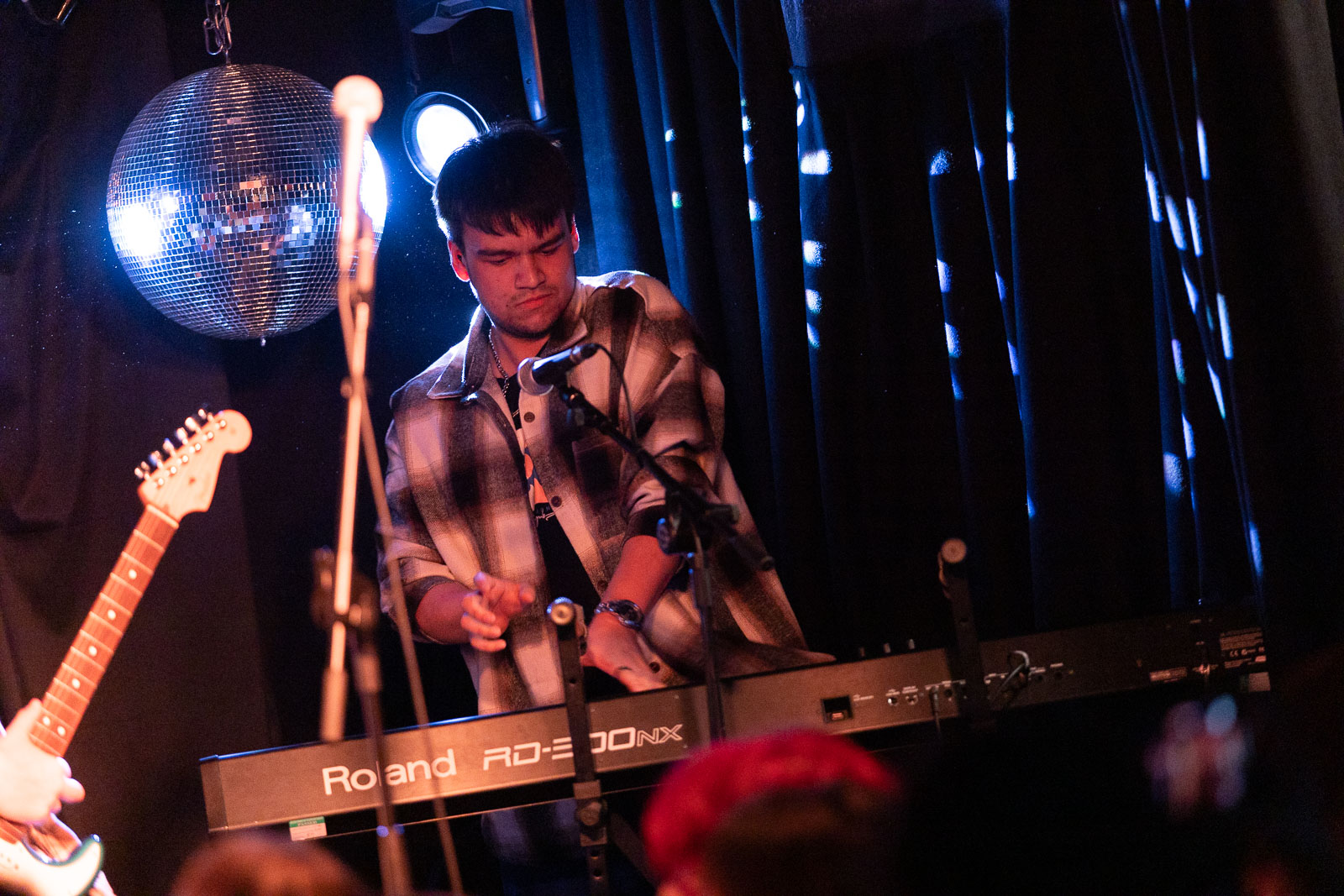 Keyboard player performing as part of a band  on stage with a disco ball behind them.