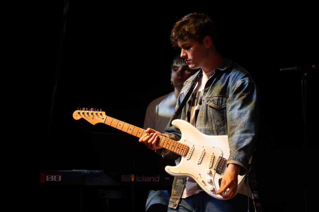 Guitarist performs on stage, looking down at his guitar.