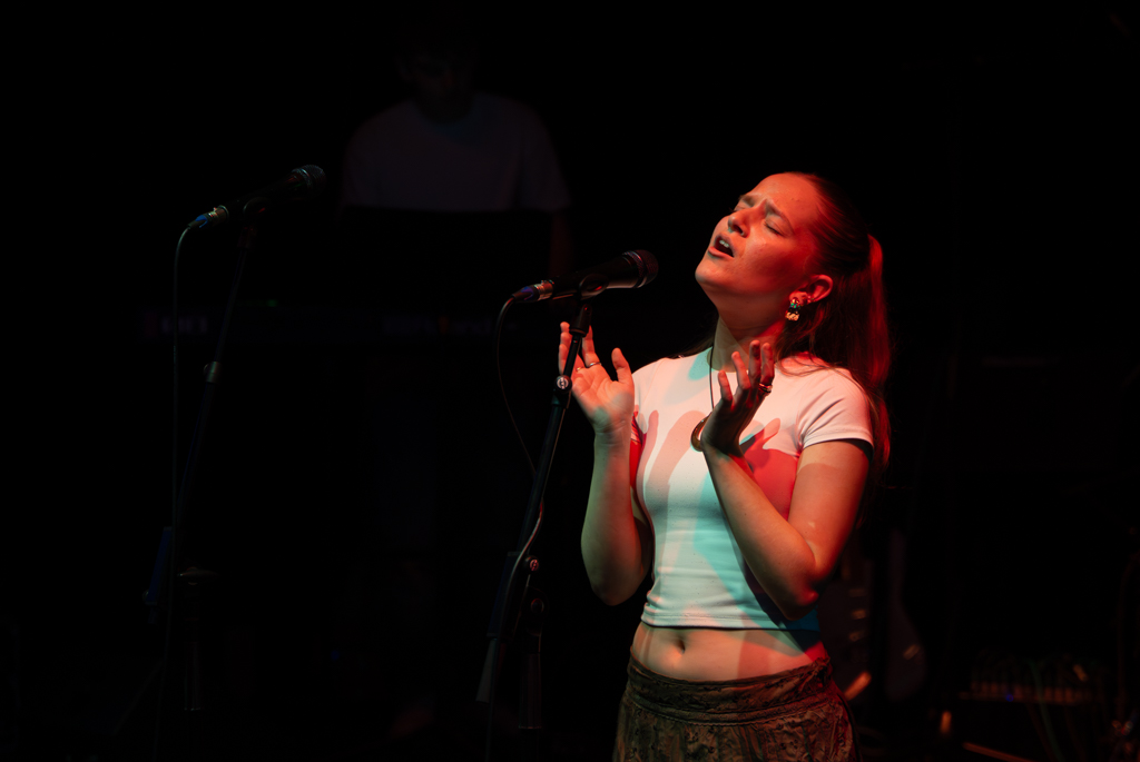 Solo singer performs with her eyes closed and palms raised to the ceiling.