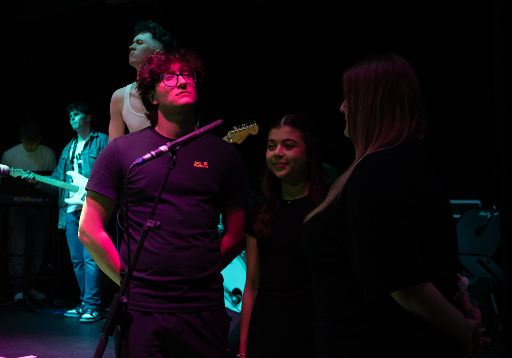 Three singers stand around a mic as they support the band.
