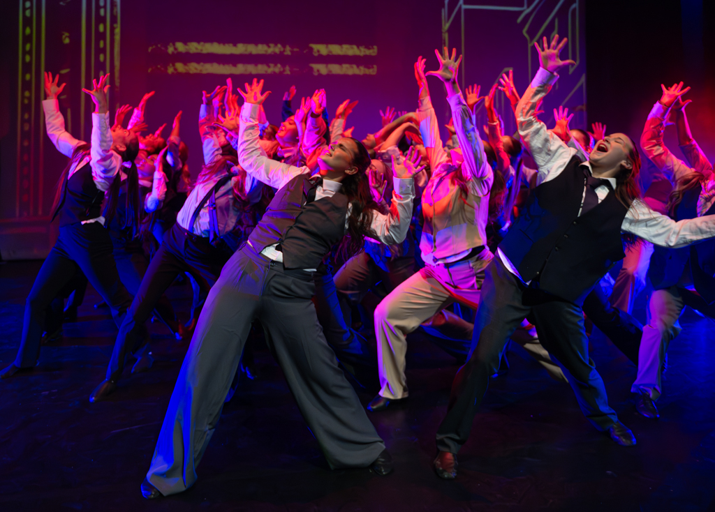 Dance students stood in the same pose with their arms in the air whilst singing.