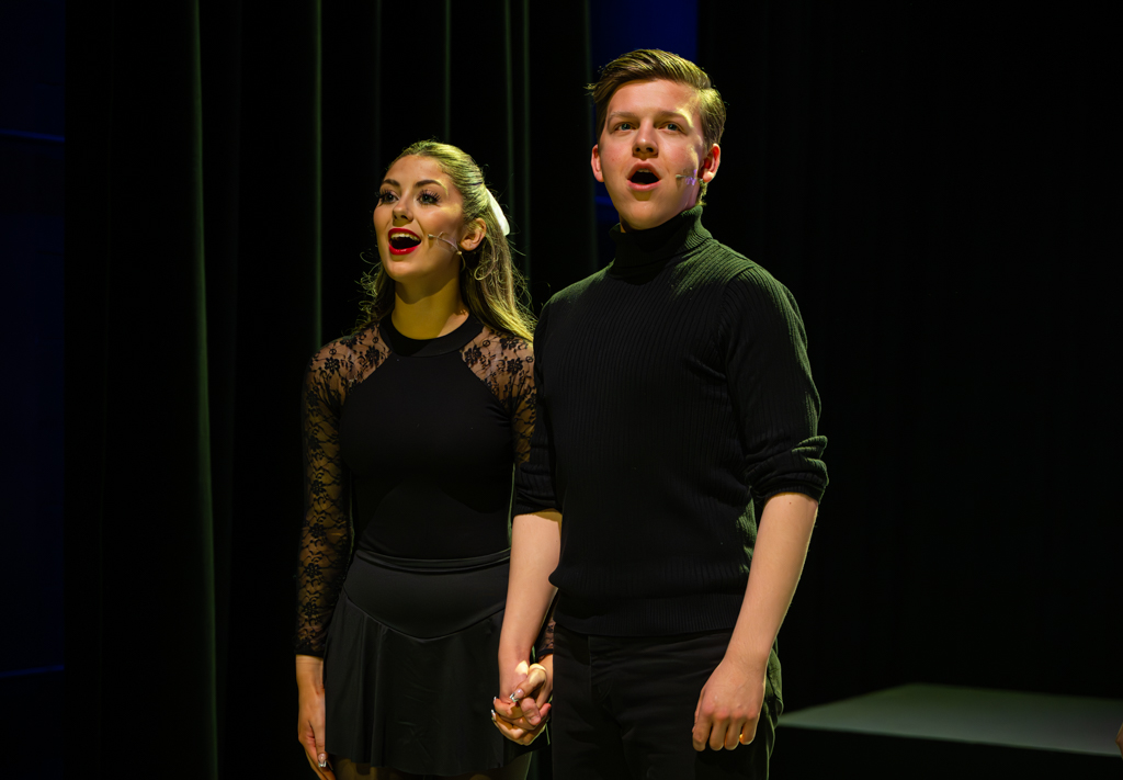 Two students sing whilst holding hands. 