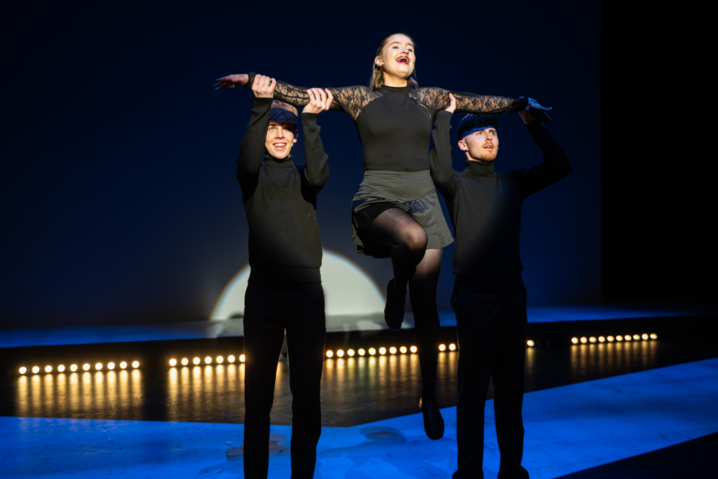 Two students hold another up in the air by their arms as they sing.