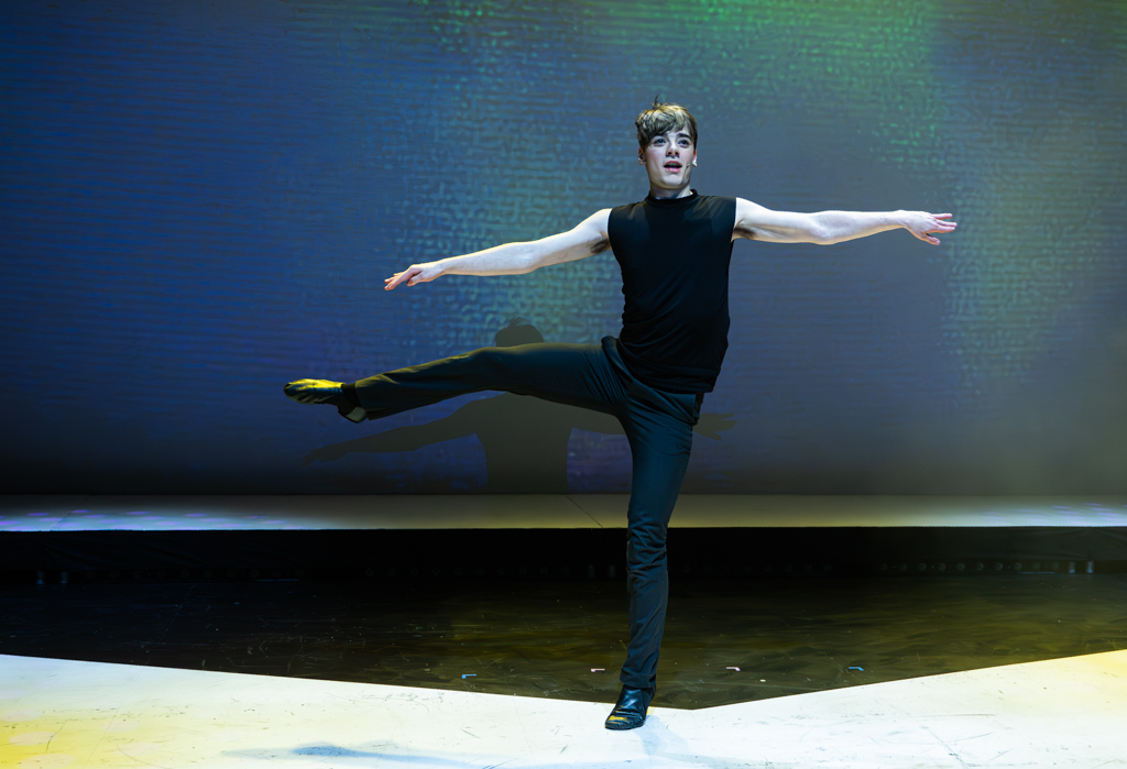 A student kicks one leg out to the side of them whilst looking to the audience.