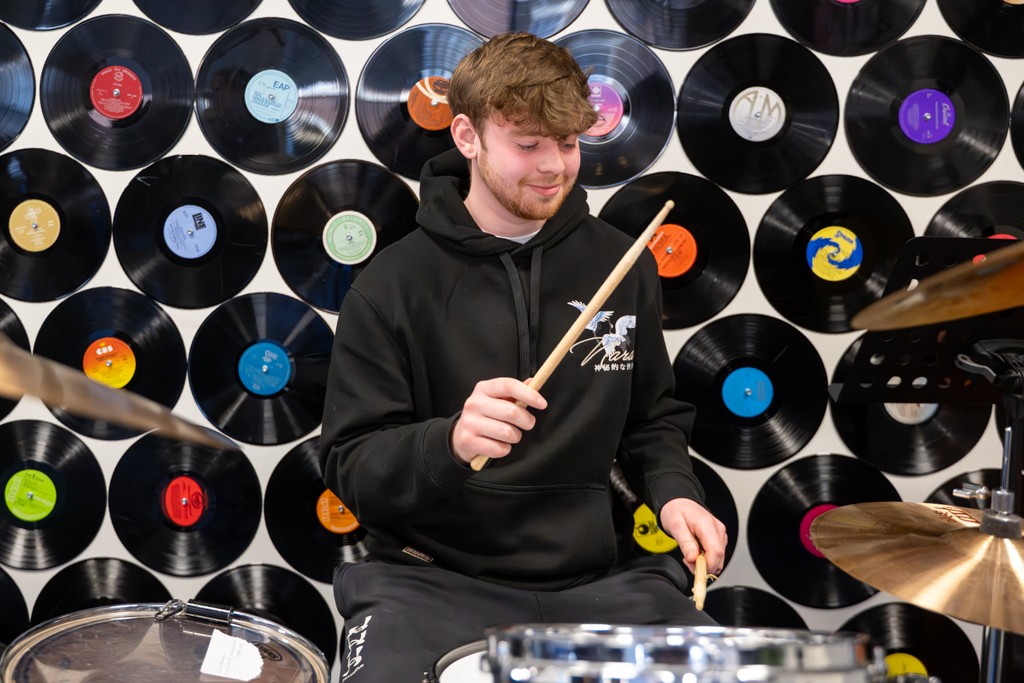Student plays the drums infront of a wall decorated with vinyl records