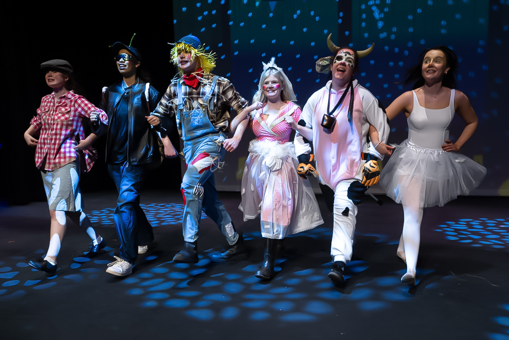 Students in costume linking arms walking forward in a performance.