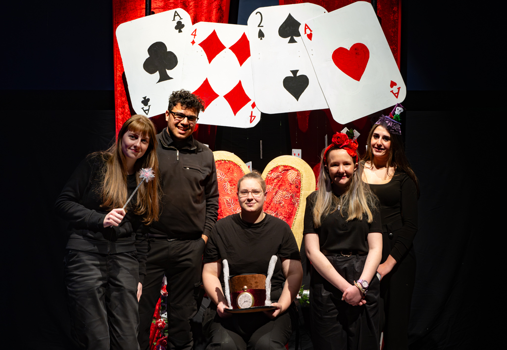 Students sat around a throne which is decorated with playing cards and a red curtain behind.