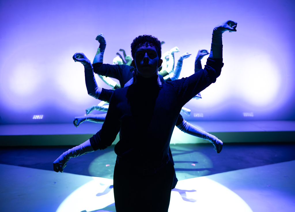Many students dancing on stage, all in the same pose with their arms bent.