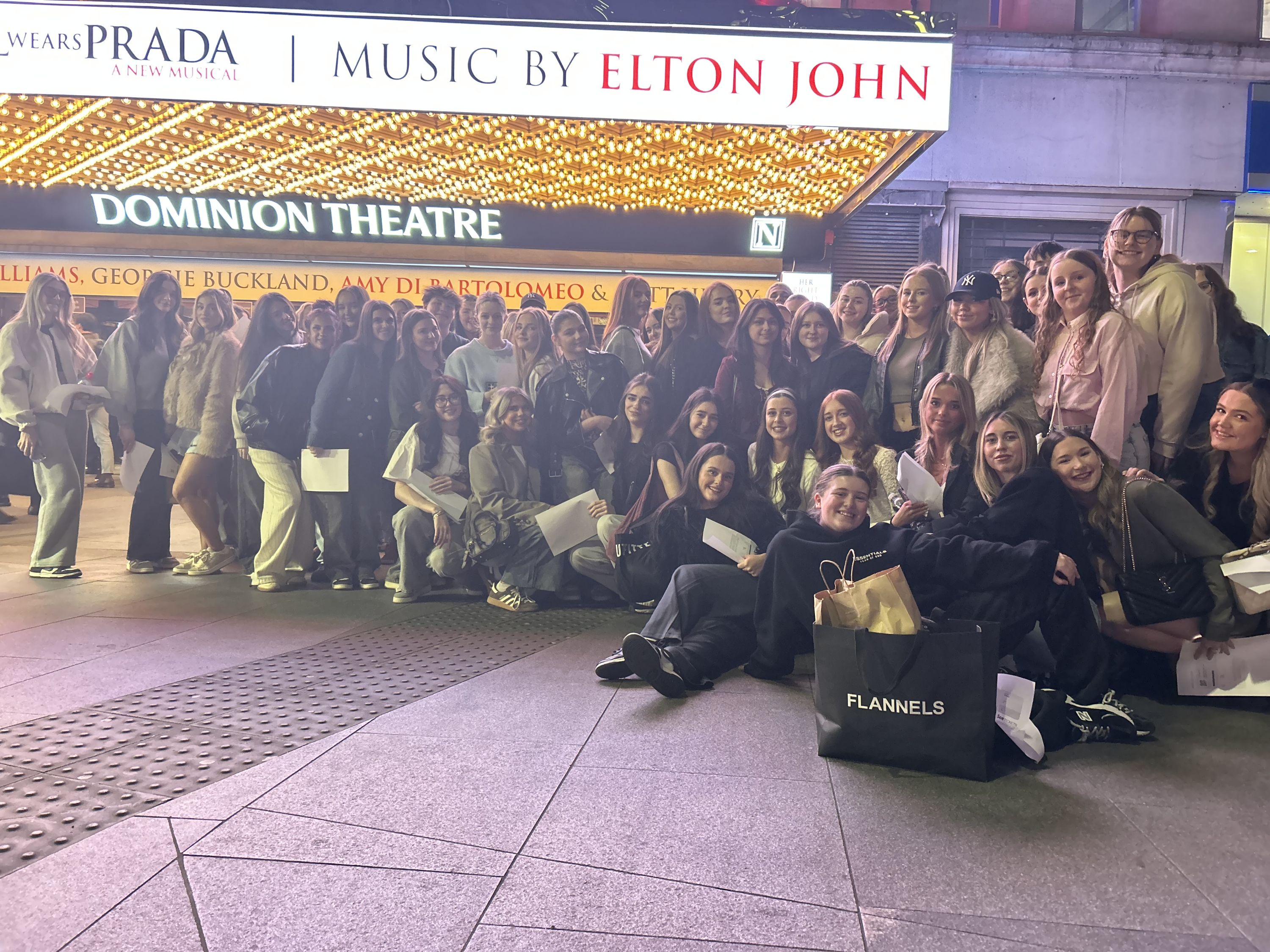 Students stand together outside Theatre on a trip.